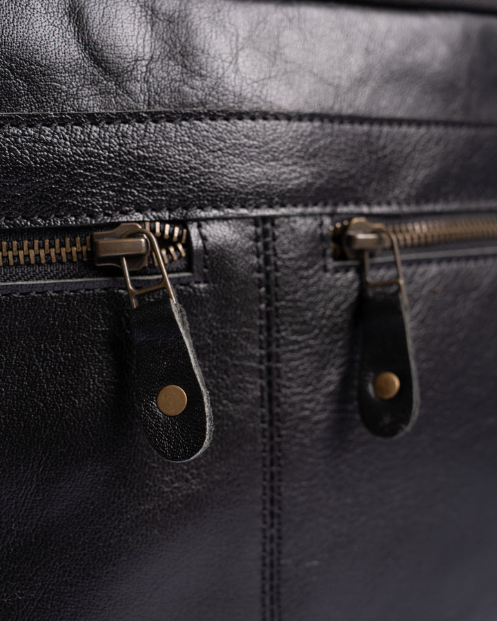 Close-up of a black leather bag with gold zipper pulls.