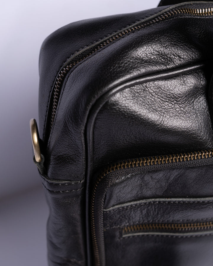 Close-up of a black leather bag with gold zippers on a light purple background